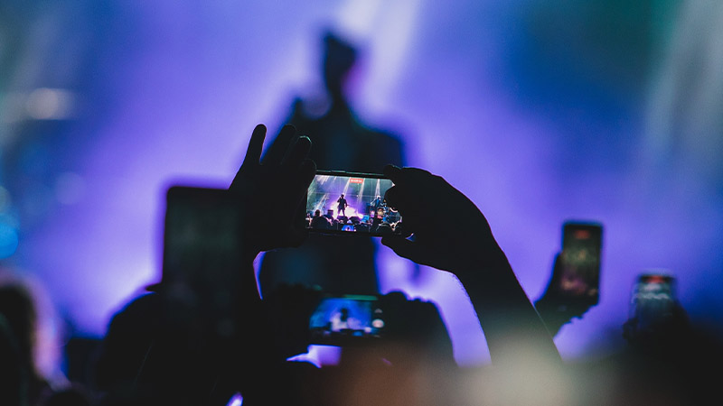 A person holding a cell phone with a band performing on stage